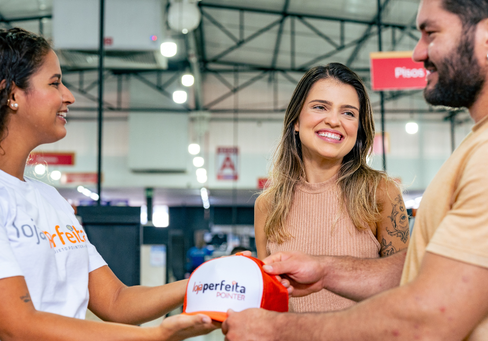 Vendedora presentando casal com boné em uma loja de materiais de construção