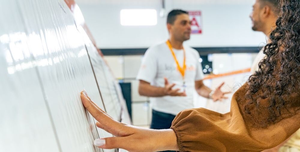 Mulher tocando revestimento em loja de materiais de construção. O rosto dela não aparece. Ao fundo da imagem aparece um vendedor