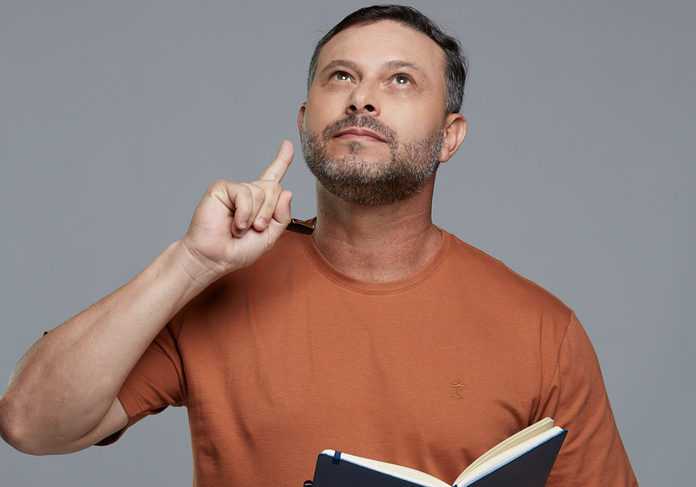 Homem segurando caderno e olhando para cima enquanto pensa